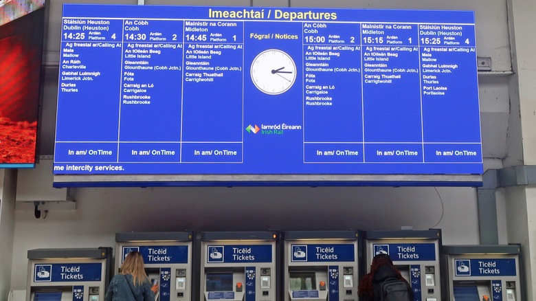 LED screen displaying train departure times and destinations hangs above ticket kiosks