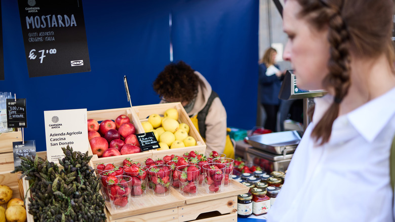 woman looking at a farmers' market booth with strawberries, apples, jams
