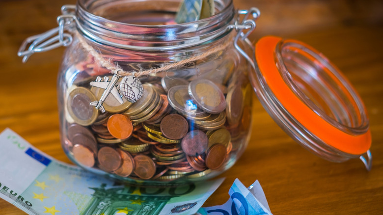 A jar full of Euro coins with Euro bills on a table.