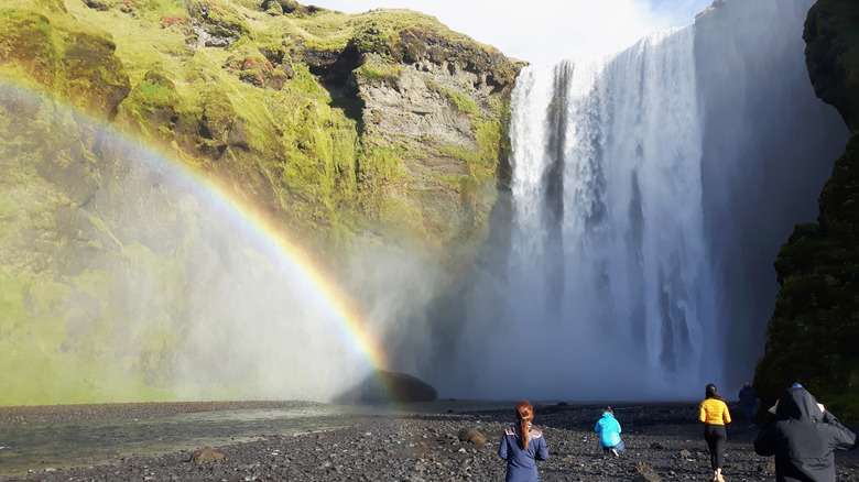 An image of a waterfall in Iceland with a rainbow and tourists walking around