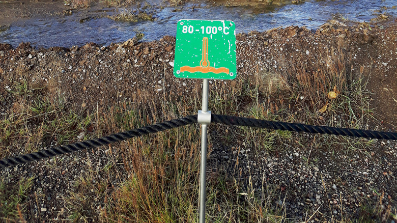 A sign in front of a geyser stating a temperature warning of 80 to 100 degrees Celsius