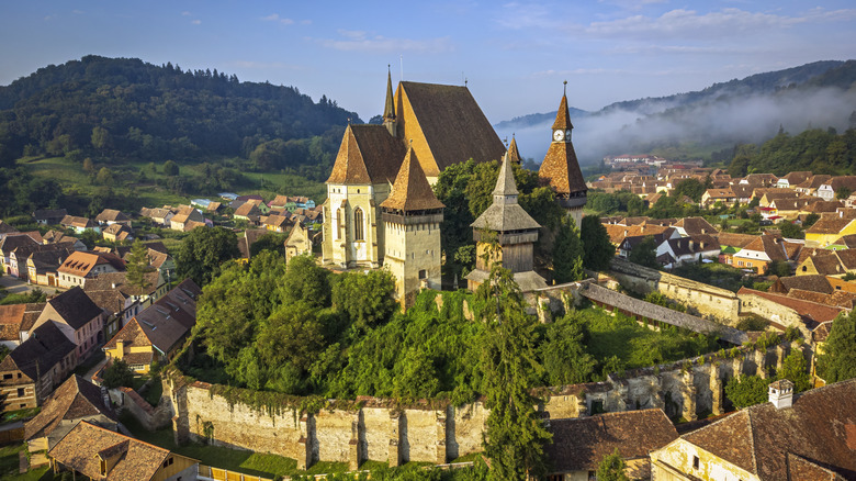 A medieval church sits on a hilltop above a small village in rural Romania.
