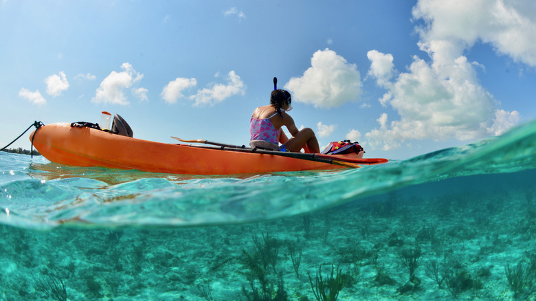 A person wearing snorkeling gear in an orange kayak on clear green water in Turks and Caicos.