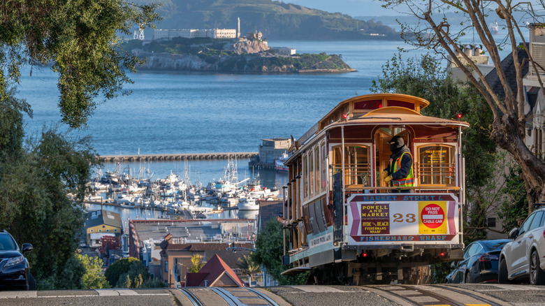 San Francisco cable cars going up a hill with Alcatraz in the background