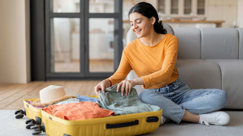woman sitting on floor packing suitcase
