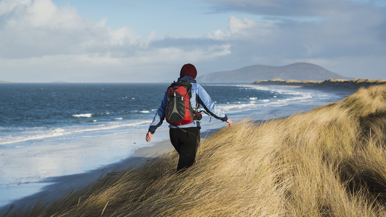 A hiker trudges through sea grasses in Berneray, Scotland