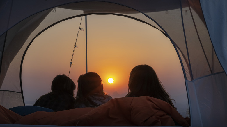 silhouettes of three people waking up in tent to sunrise