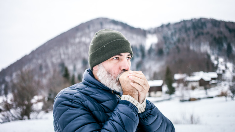 A man tries to warm his cold hands by blowing on them.