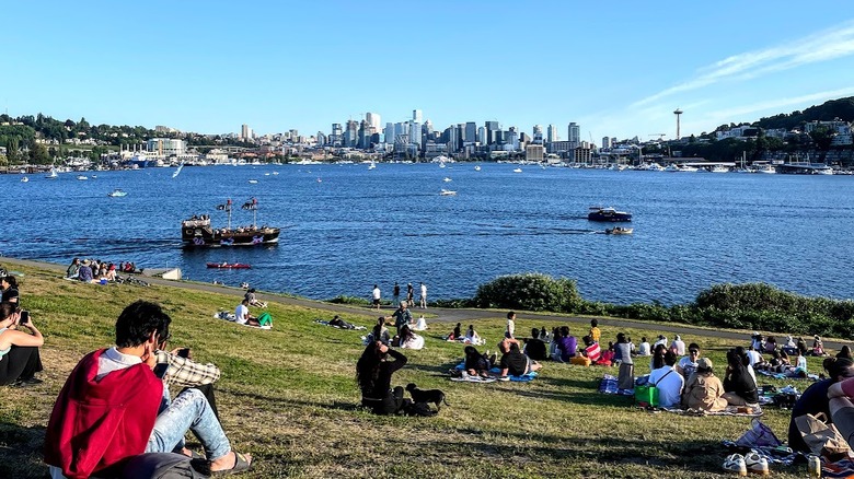 Sloped lawn with people, bay of water with boats and skyline