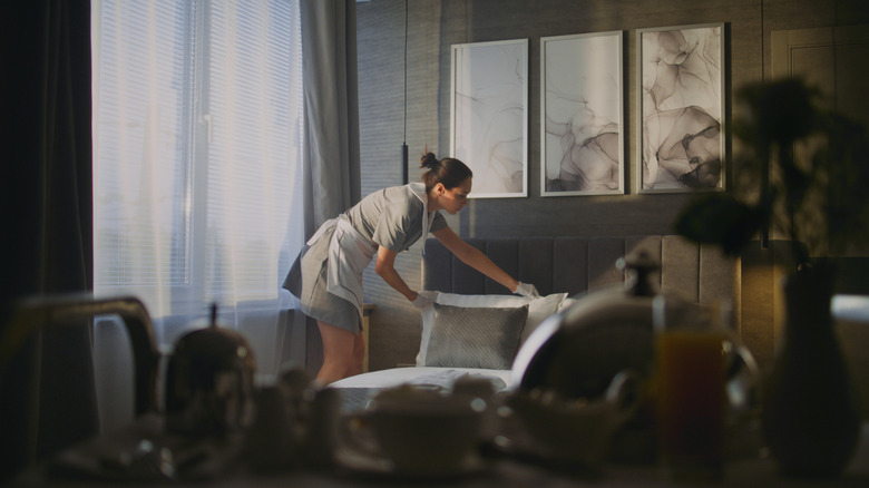 Housekeeper arranging pillows and smoothing out sheets on bed in hotel room