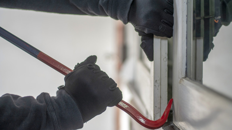 A burglar uses a crowbar to break into a house