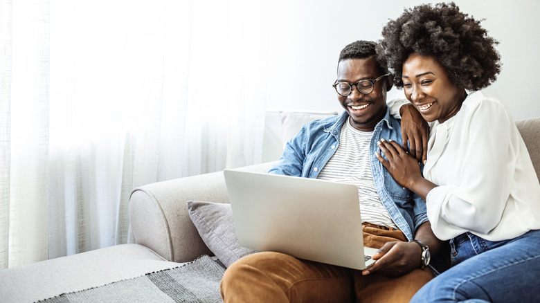 A couple looks affectionately at a computer while seated on a sofa