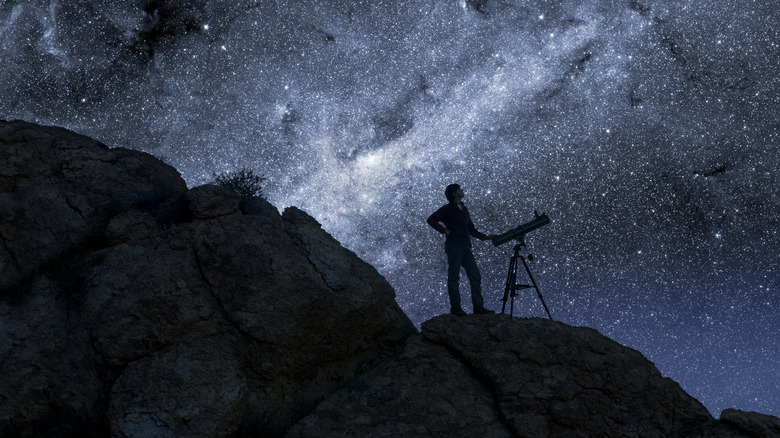 person stands next to telescope at night under starlit sky