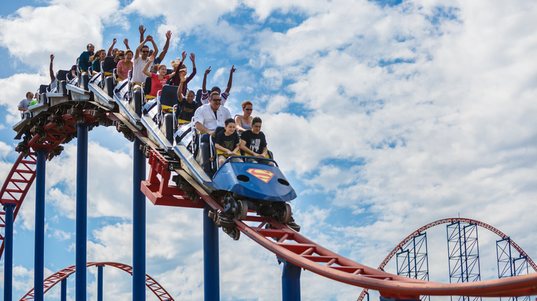 People riding a rollercoaster with a cloudy blue sky background.