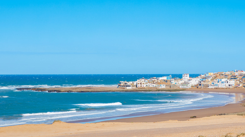 Curve of golden beach against blue sea with white village in the background