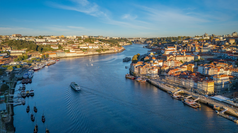 Drone view of Douro River between Porto Ribeira and Vila Nova de Gaia, Portugal, with a tourist boat and moored rabelo boats at sunrise