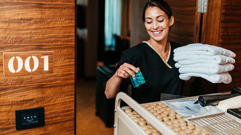 smiling housekeeper holding towels and shampoo