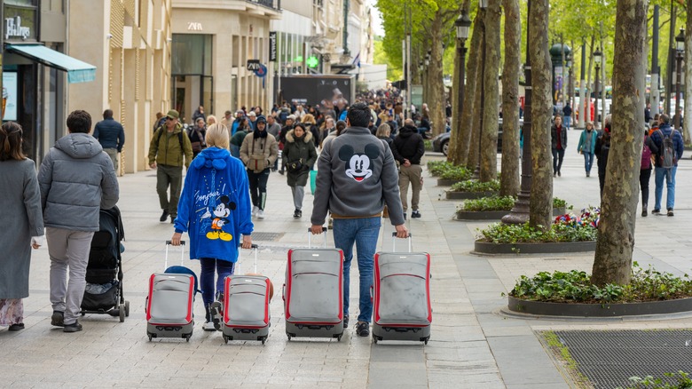 Two people in Disney sweatshirts walking with suitcases