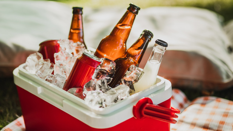 A red cooler with cans and bottles in ice.