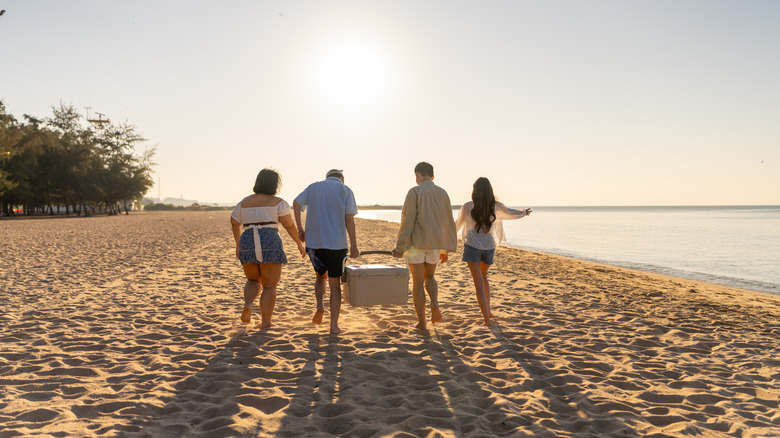 Four people on a sandy beach with two carrying a cooler.