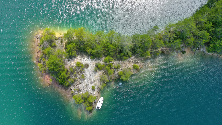 an overhead view of an island surrounded by turquoise water with a boat by the shore