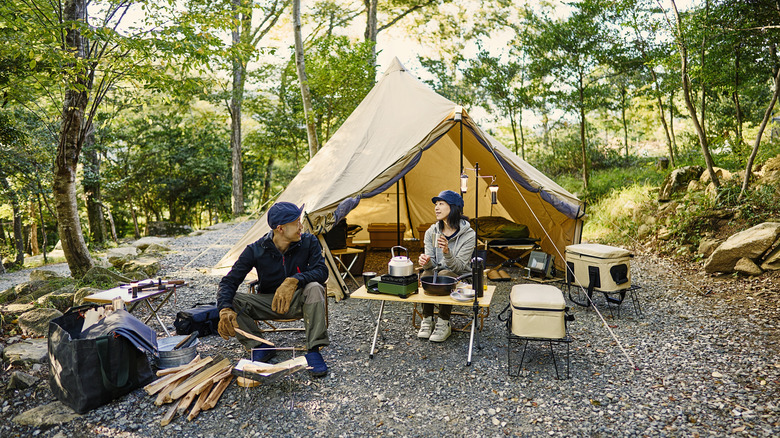 A man and woman relaxing in front of a tent at a campsite.