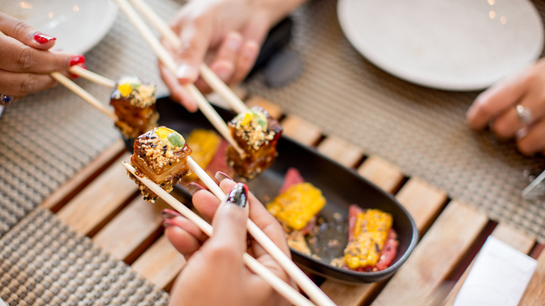 friends sharing a sushi platter in a restaurant using chopsticks