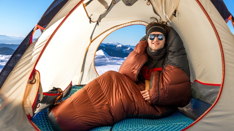 A man in a sleeping bag and tent in the snow