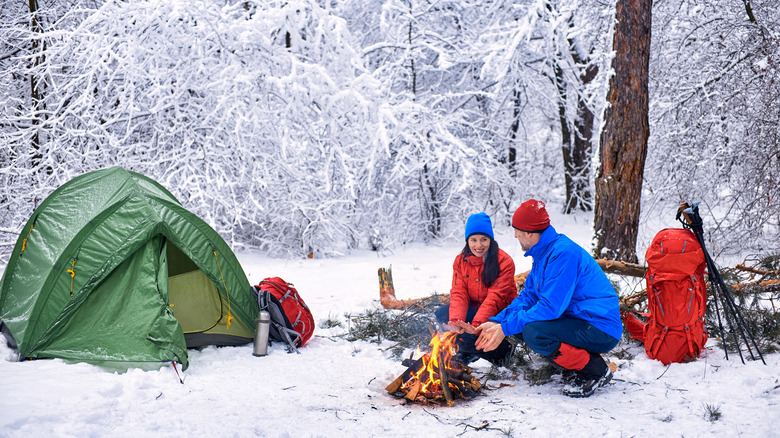 A couple camping in the snow with winter gear and a tent.