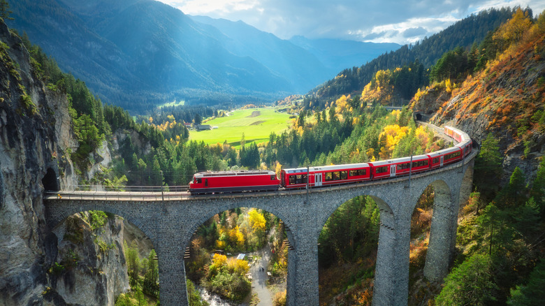 A red train on Landwasser viaduct among alpine mountains and colorful forest at sunset