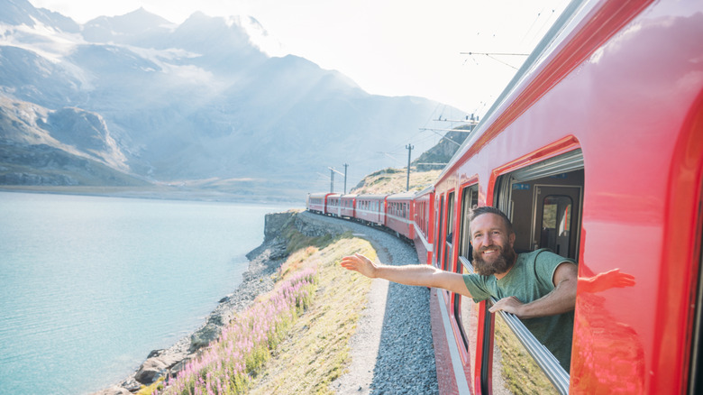 Smiling bearded man leaning out of red train window waving