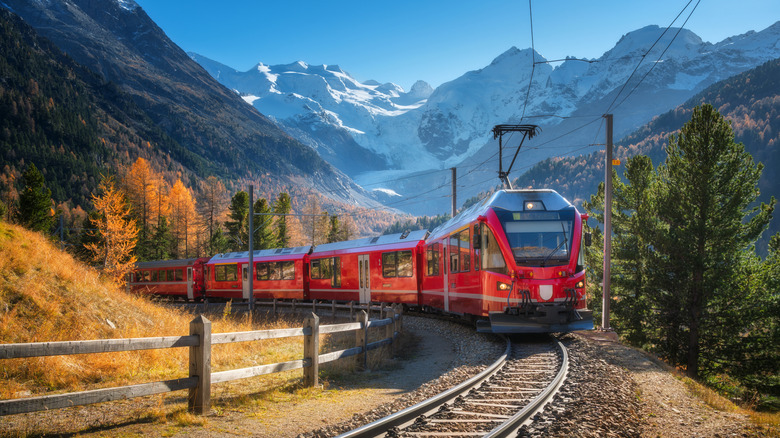 Red modern electric train with snow-capped peaks and vibrant autumn trees in Switzerland