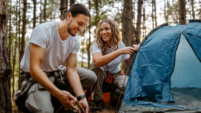 Young couple setting up a tent at a wooded campsite
