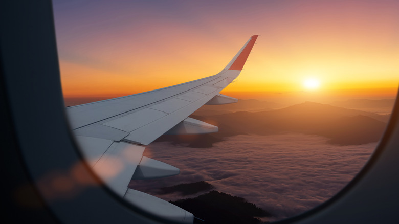 Airplane flying low over foggy mountains, view from plane window of plane wing and sky sunrise