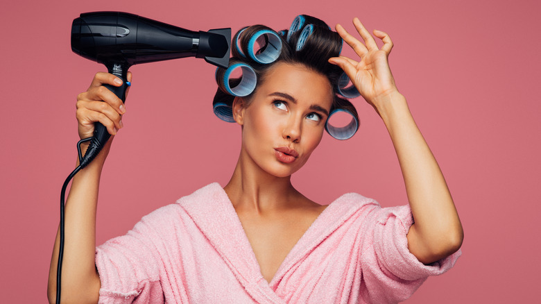 Young woman with oversized curlers in her hair holding a hairdryer
