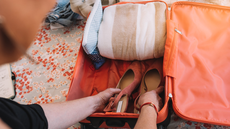 A woman's hands placing shoes inside a suitcase.