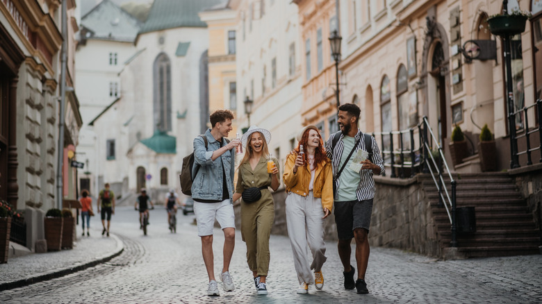 A front view of group of happy young people with drinks outdoors on street on town trip, laughing.
