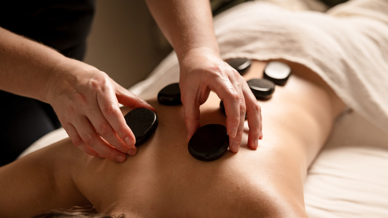 A massage therapist places hot stones on a client's back during a stone therapy session