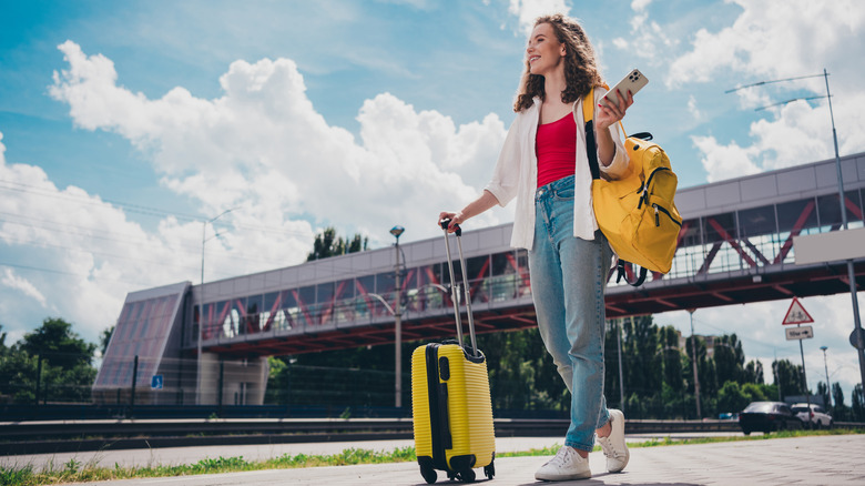 Woman smiling holding her phone and luggage