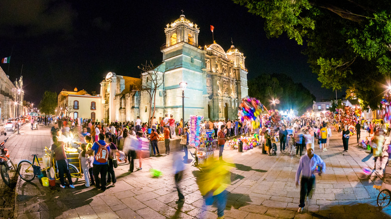 View of people walking around the lively facade of Cathedral of Our Lady of the Assumption (Catedral de Oaxaca) in Oaxaca, Mexico.