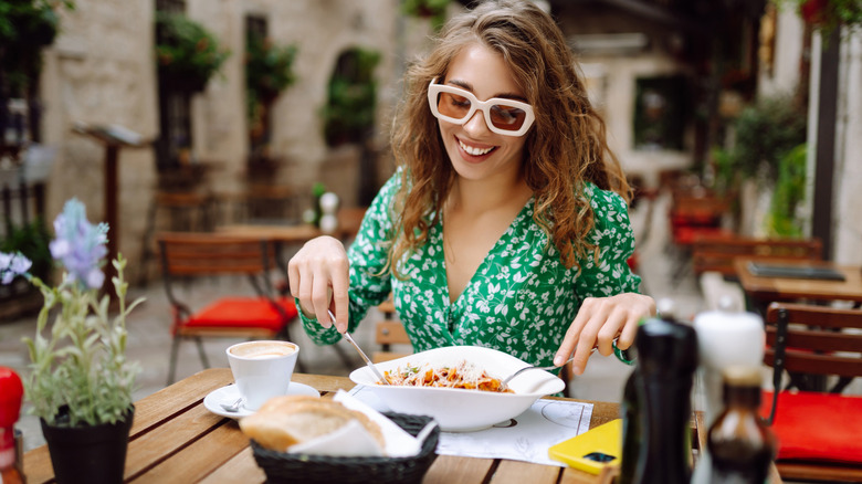 A smiling woman with trendy glasses eats a meal in an Italian restaurant