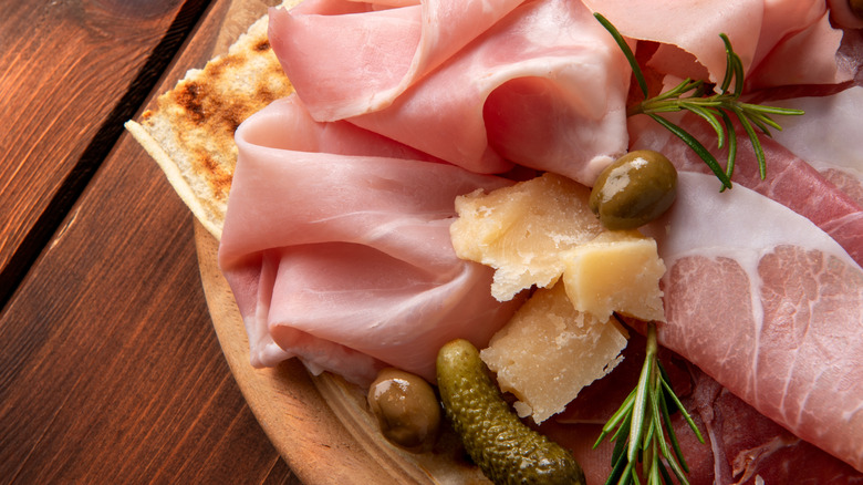 Slices of prosciutto, cheese, and olives lie on a wood board