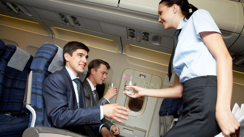 A flight attendant giving a passenger a cup of water.