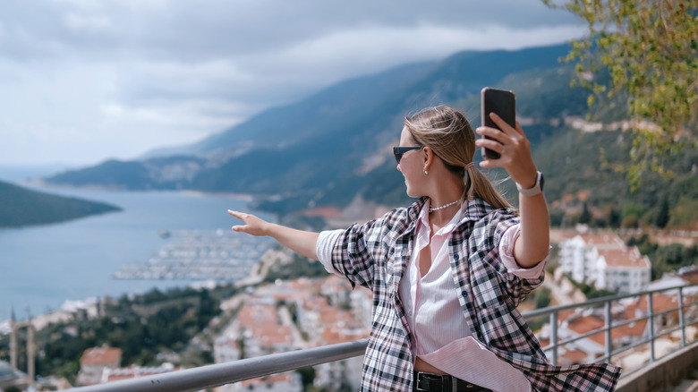 woman holding up her phone while looking out over a city and waterway