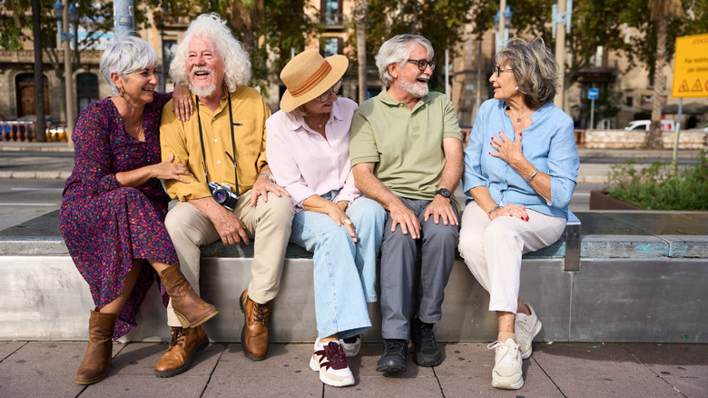 five elderly people smiling and chatting while sitting on a concrete bench