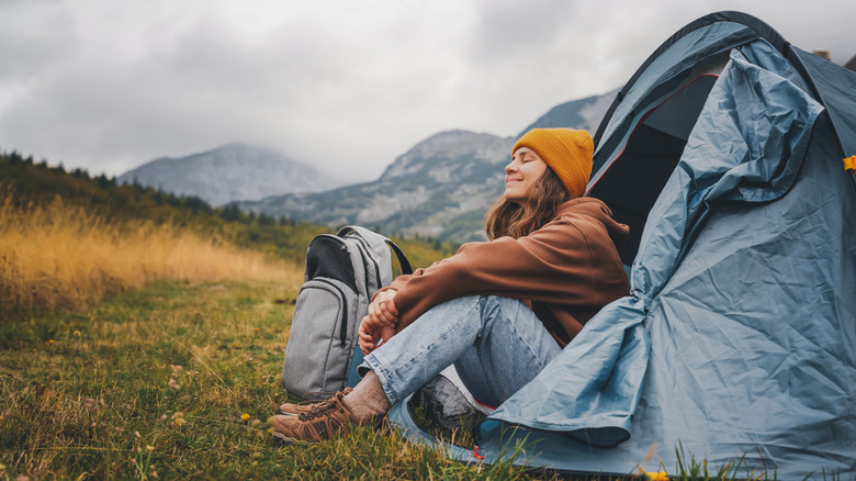 a woman solo camping, sitting at the entrance to her tent and enjoying the fresh air and solitude