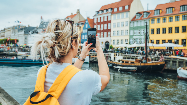 Woman taking a photograph on her phone of Nyhaven in Copenhagen