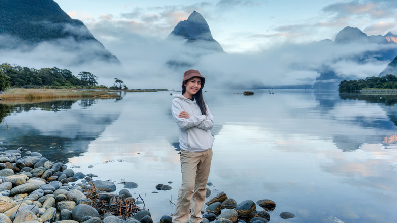 Happy female tourist in front of Milford Sound and a foggy lake at Fiordland National Park, New Zealand