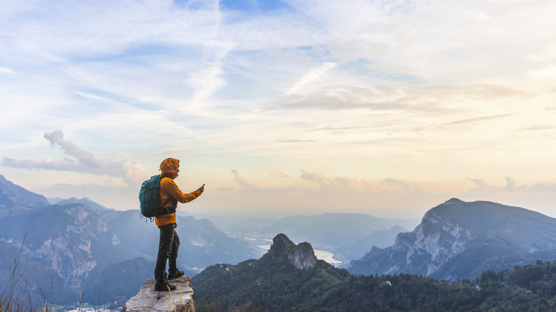 A hiker on top of a mountain looks at their phone.