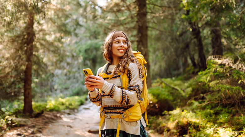 A woman on a forest trail using a navigation app on her phone.